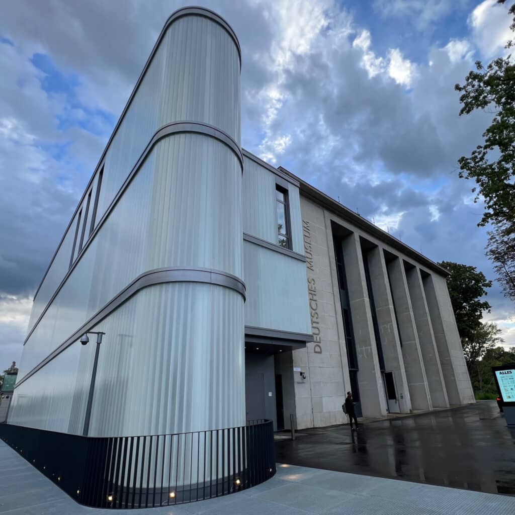 Moderne Architektur des Deutschen Museums in München mit geschwungener Glasfassade und Eingangsbereich, bewölkter Himmel im Hintergrund.