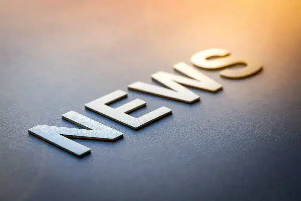 3D-Schriftzug "NEWS" auf einer grauen Oberfläche in einem sanften Lichtstrahl.
