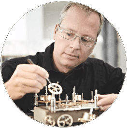 Eine Person bestückt ein Uhrwerk mit Zahnrädern, konzentriert sich dabei auf präzise Details.