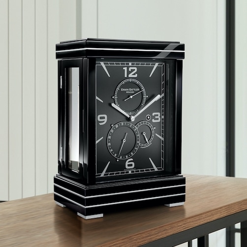 Schwarze Tischuhr Metrica II von Erwin Sattler mit Metallintarsien im Gehäuse auf einem Holztisch, modernes Design mit großen weißen Ziffern.
