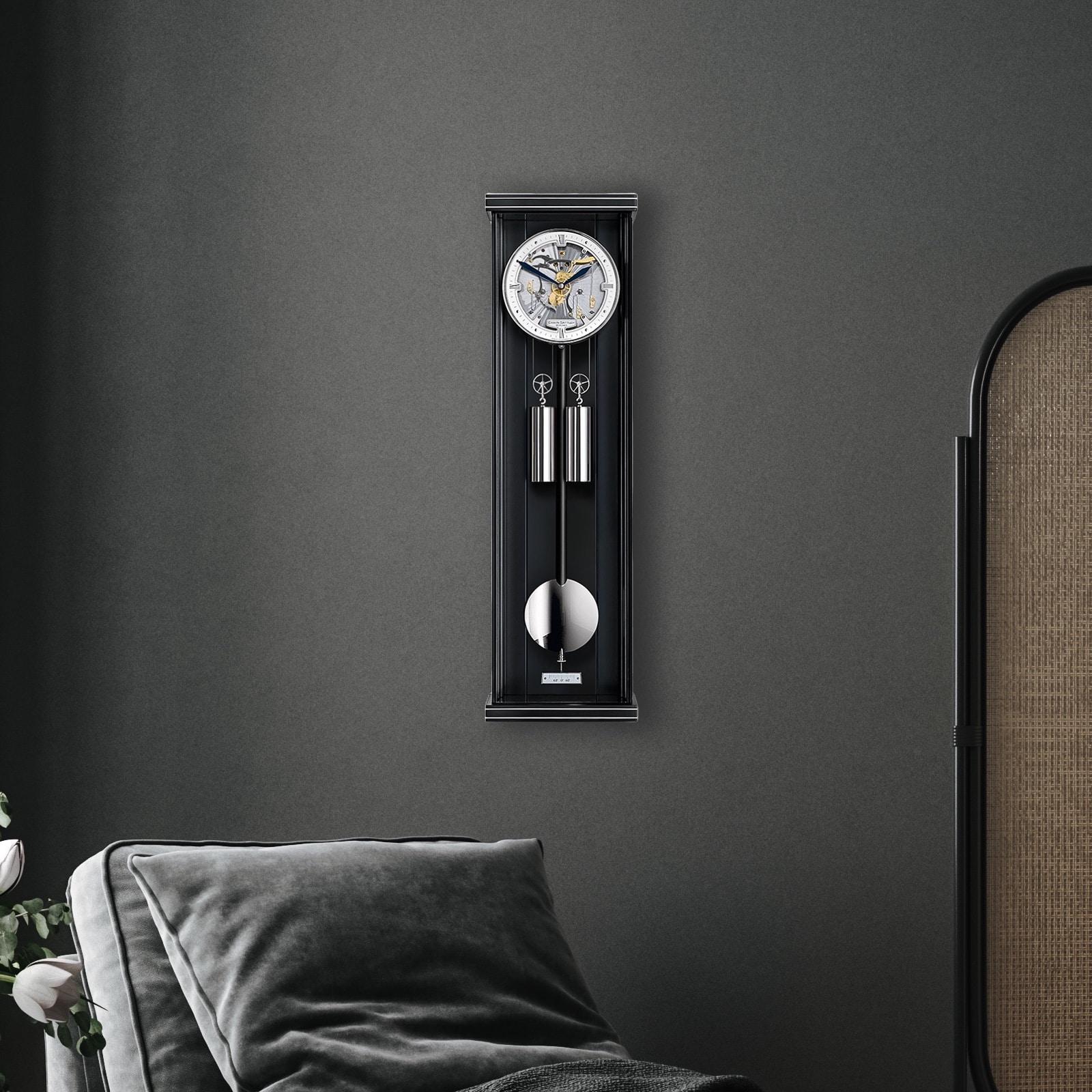 Wandpendeluhr Aperia S70 von Erwin Sattler mit skelettiertem Zifferblatt und silbernen Details vor einer grauen Wand, im Hintergrund ein Teil eines grau gepolsterten Sofas und eine Pflanze.