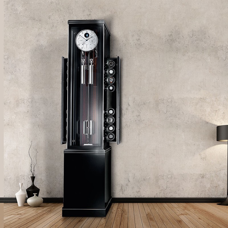 Schwarze Standuhr Troja Opus Temporis von Erwin Sattler mit silbernen Pendeln und Zifferblättern an einer Betonwand, umgeben von schlichter Dekoration und einem Holzfußboden.