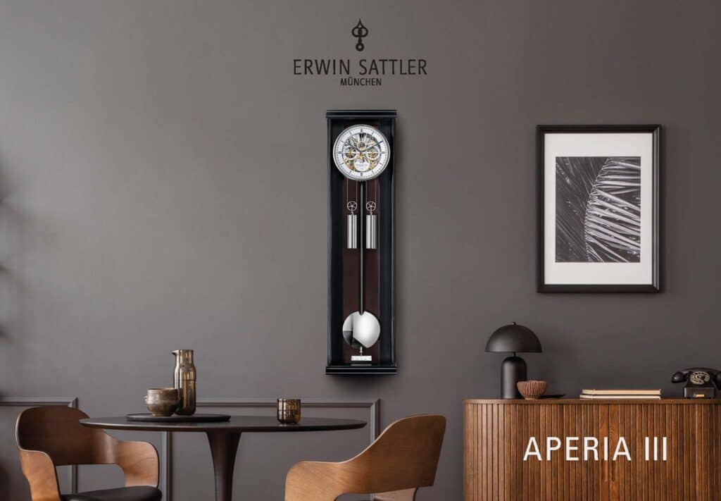 Moderne Inneneinrichtung mit hölzernem Tisch und braunen Stühlen vor einer grauen Wand, an der die elegante Pendeluhr Aperia III von Erwin Sattler und ein abstraktes Kunstwerk hängen. Daneben ein hölzernes Sideboard mit Lampe, Telefon und Büchern.