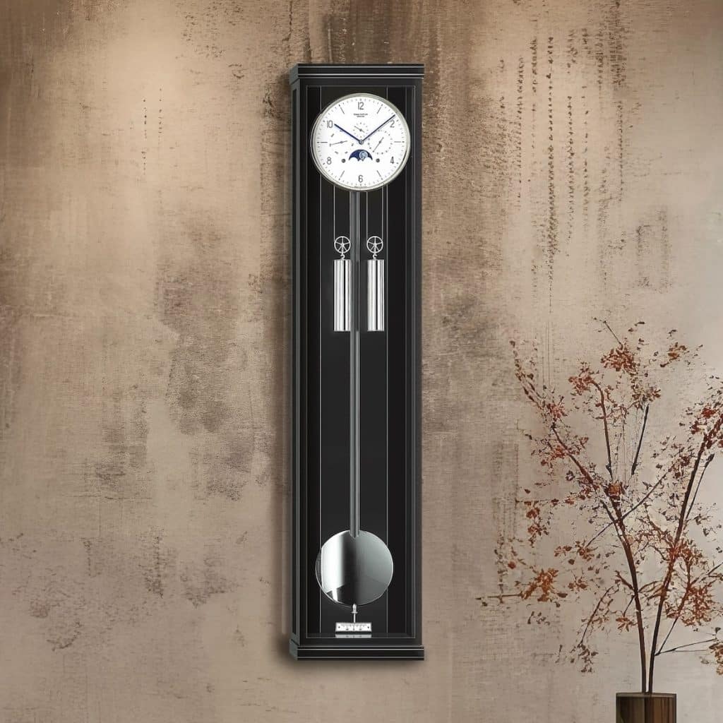 Wanduhr Classica KS130M in schwarz von Erwin Sattler hängt an einer braunen Betonwand. Eingangsbereich mit grauen Stufen und einem Holztisch darunter