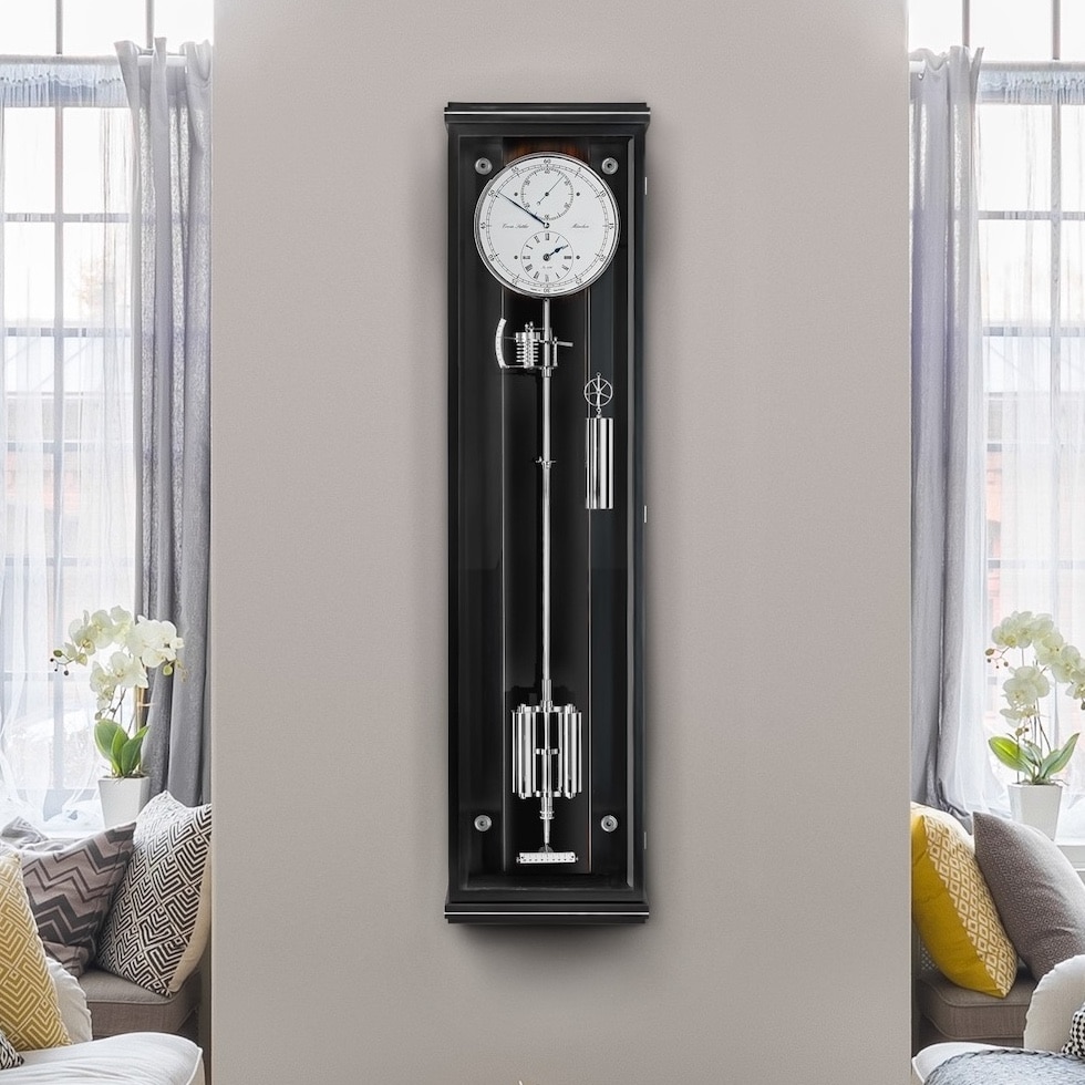 Wanduhr Classica Secunda 1985 von Erwin Sattler im klassischen Design mit schwarzem Gehäuse und sichtbarem Pendel, zwischen zwei großen Fenstern mit weißen Vorhängen.