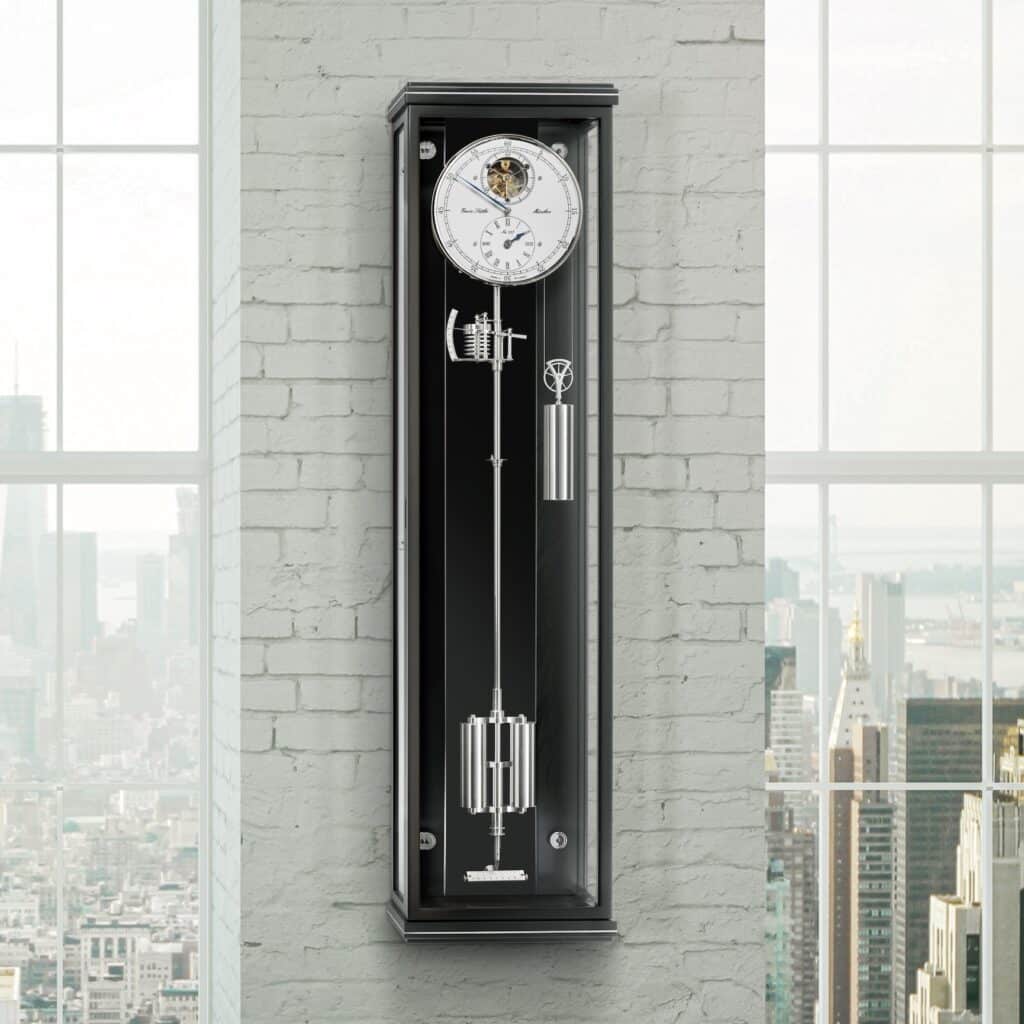 Wanduhr Classica Secunda 1995M mit sichtbarem Uhrwerk und Gewichten, montiert an einer weißen Ziegelwand, im Hintergrund Stadtansicht durch Fenster.