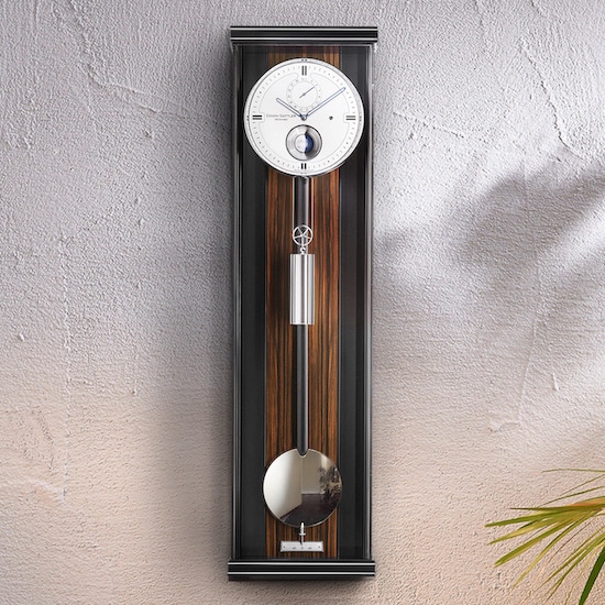 Eine modern gestaltete Wanduhr Modell Opus PMD 100 von Erwin Sattler mit langem Pendel und silbernem Ziffernblatt, montiert auf einer strukturierten Wand.