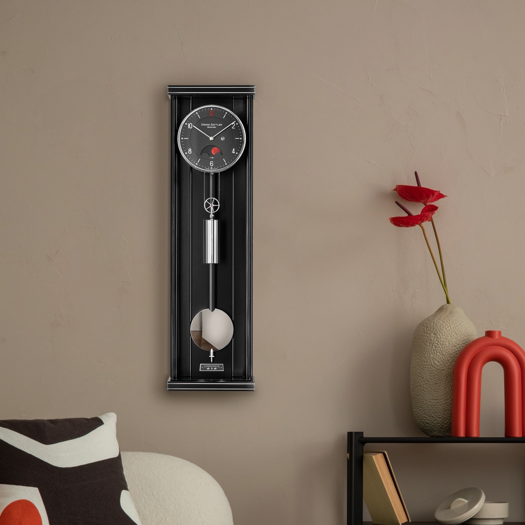 Eine schwarze Wanduhr mit Pendel, Modell Oppus P70M III von Erwin Sattler, daneben eine Vase mit roten Blumen auf einem Regal.