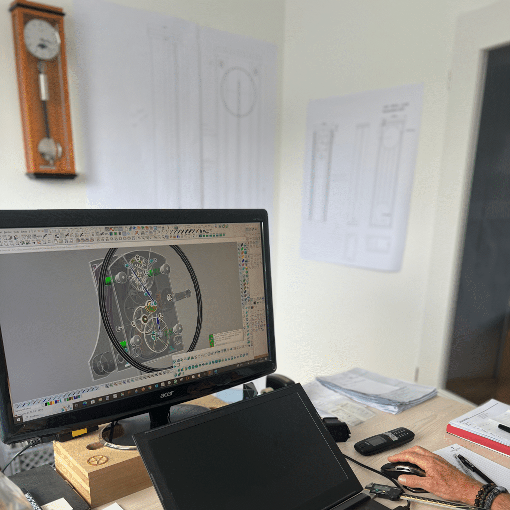 Person arbeitet an einem Computer, auf dem ein technisches CAD-Design angezeigt wird. Zeichnungen an der Wand, Laptop und Dokumente auf dem Tisch.