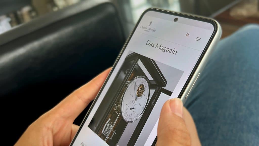 Person hält ein Smartphone, auf dem eine Webseite mit einer Standuhr angezeigt wird.