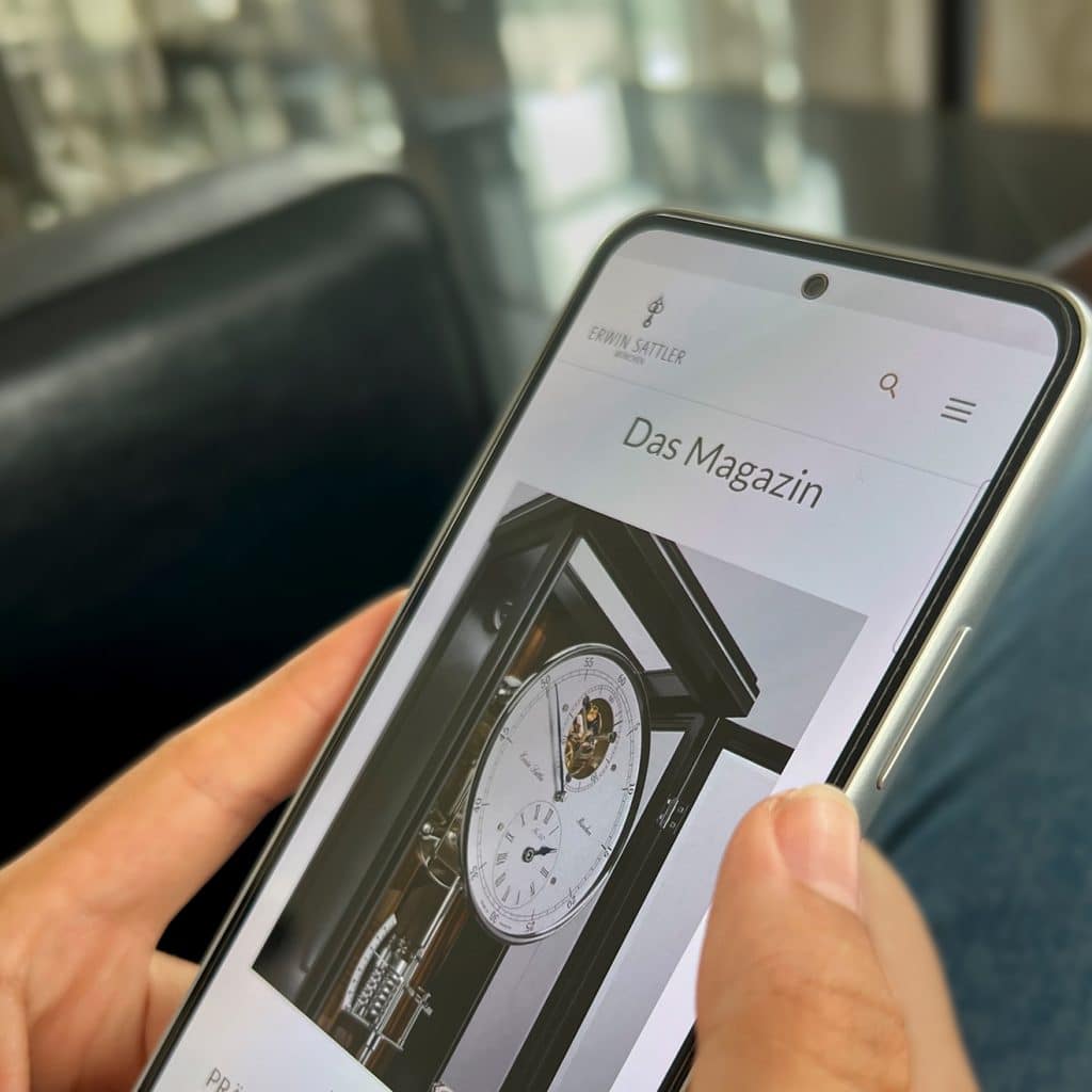 Person hält ein Smartphone, auf dem eine Webseite mit einer Standuhr angezeigt wird.