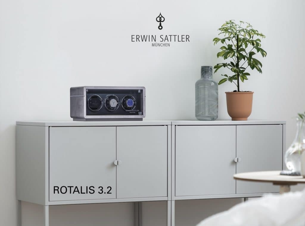 Uhrbeweger ROTALIS 3.2 auf einem weißen Schrank mit Pflanze und Glasvase daneben, Markenname ERWIN SATTLER an der Wand.