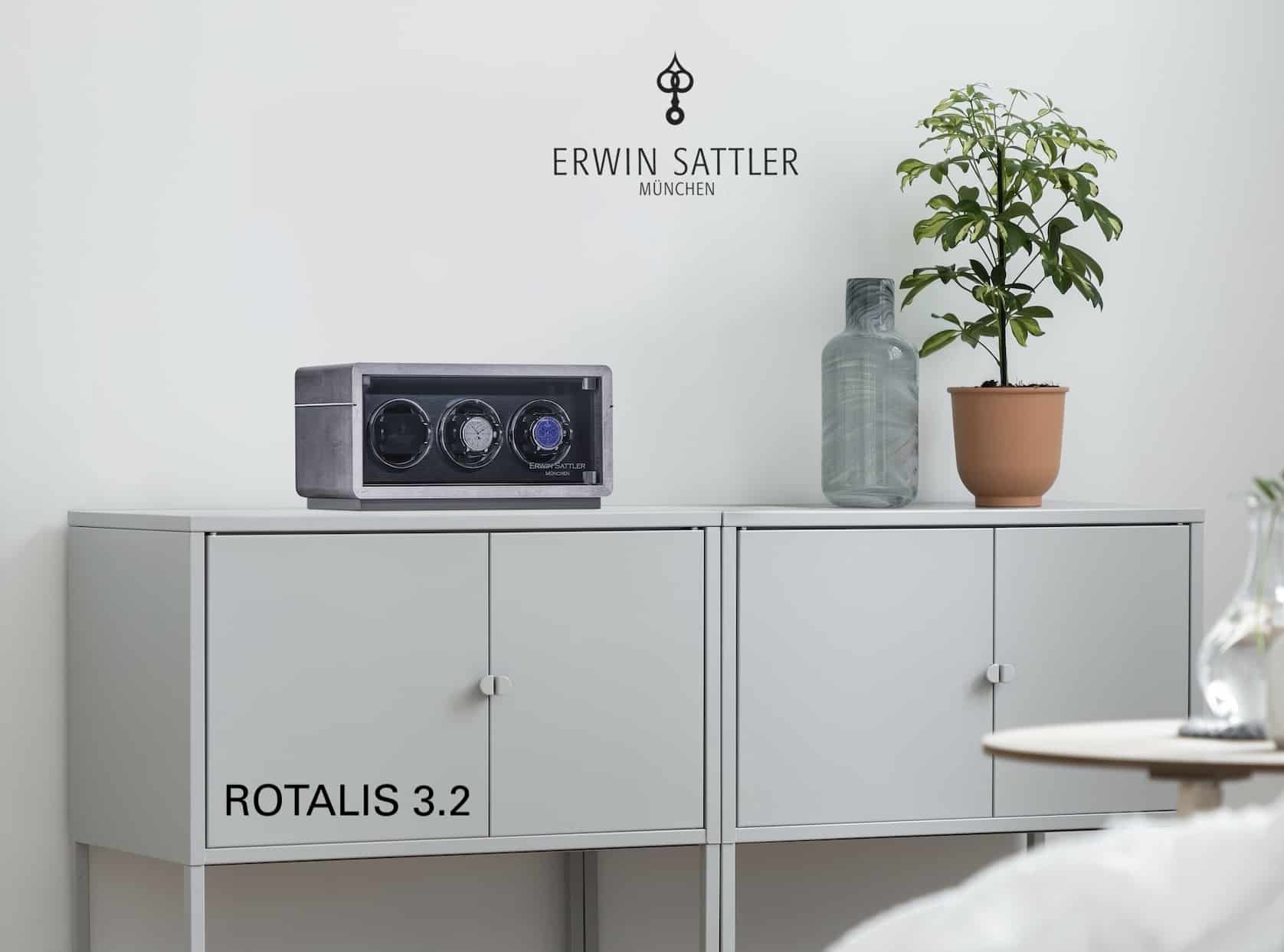 Uhrbeweger ROTALIS 3.2 auf einem weißen Schrank mit Pflanze und Glasvase daneben, Markenname ERWIN SATTLER an der Wand.