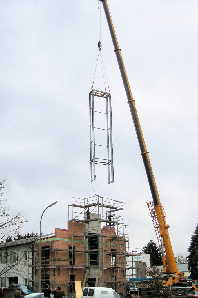 Ein Kran setzt den Rahmen der Turmuhr Monumentum Temporis vor dem Gebäude in Position.